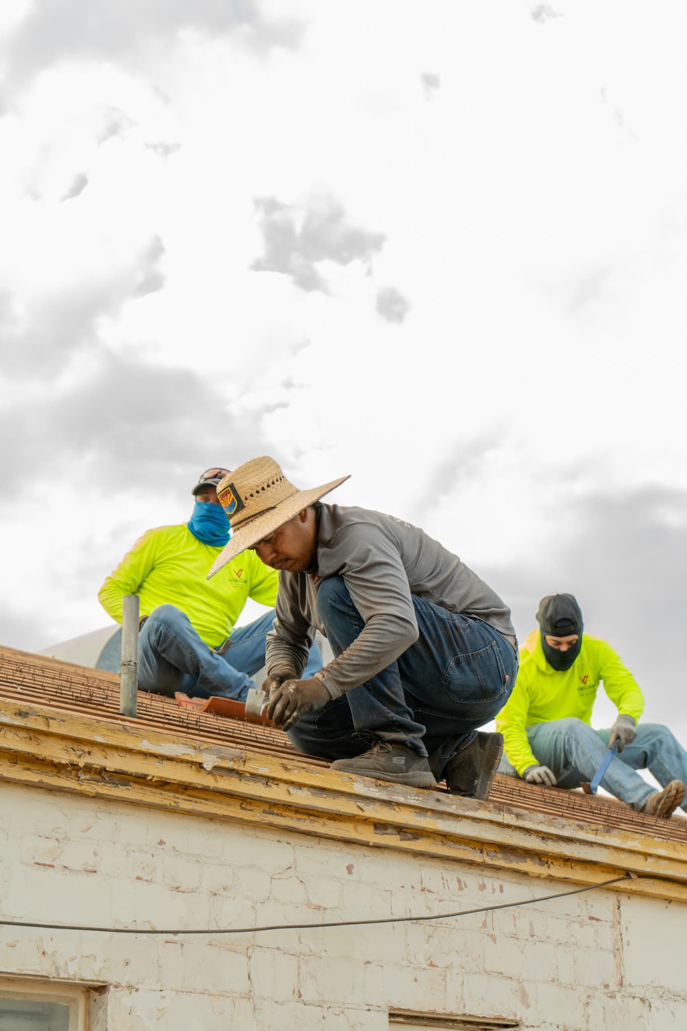 Three Vizcom Contracting roofers rebuilding the ridge of an older brick building.
