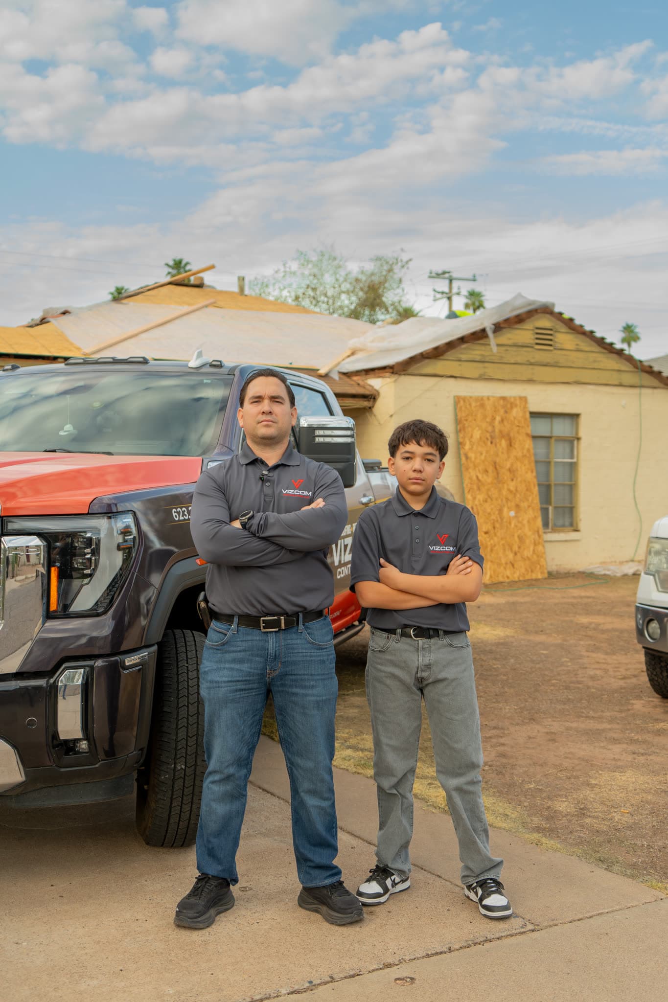 Omar Vizcarra and his son standing by a Vizcom truck at a Phoenix house with its roof opened up and a window boarded over.
