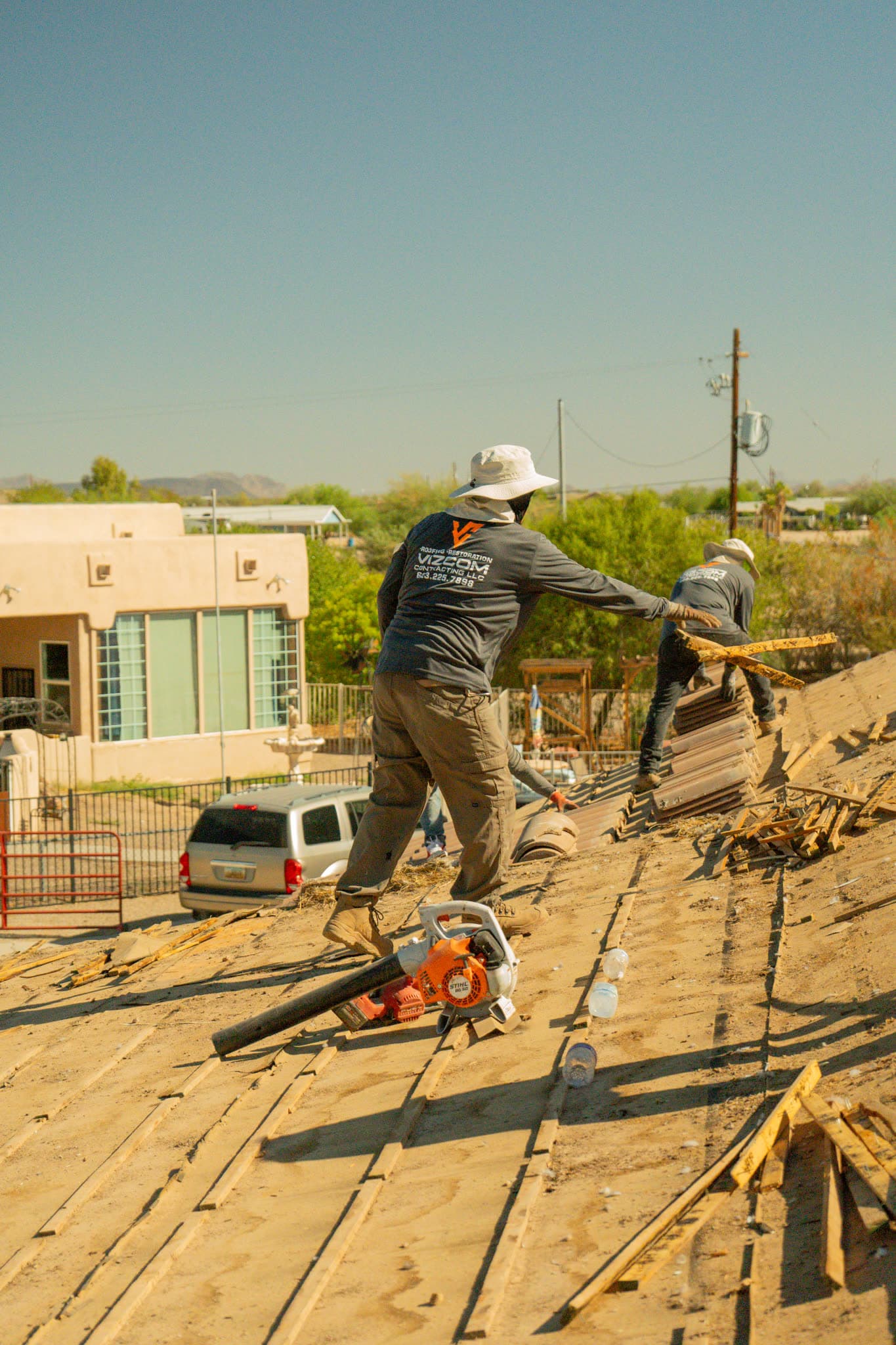 Two Vizcom Contracting roofers stripping old panels and debris off a roof.