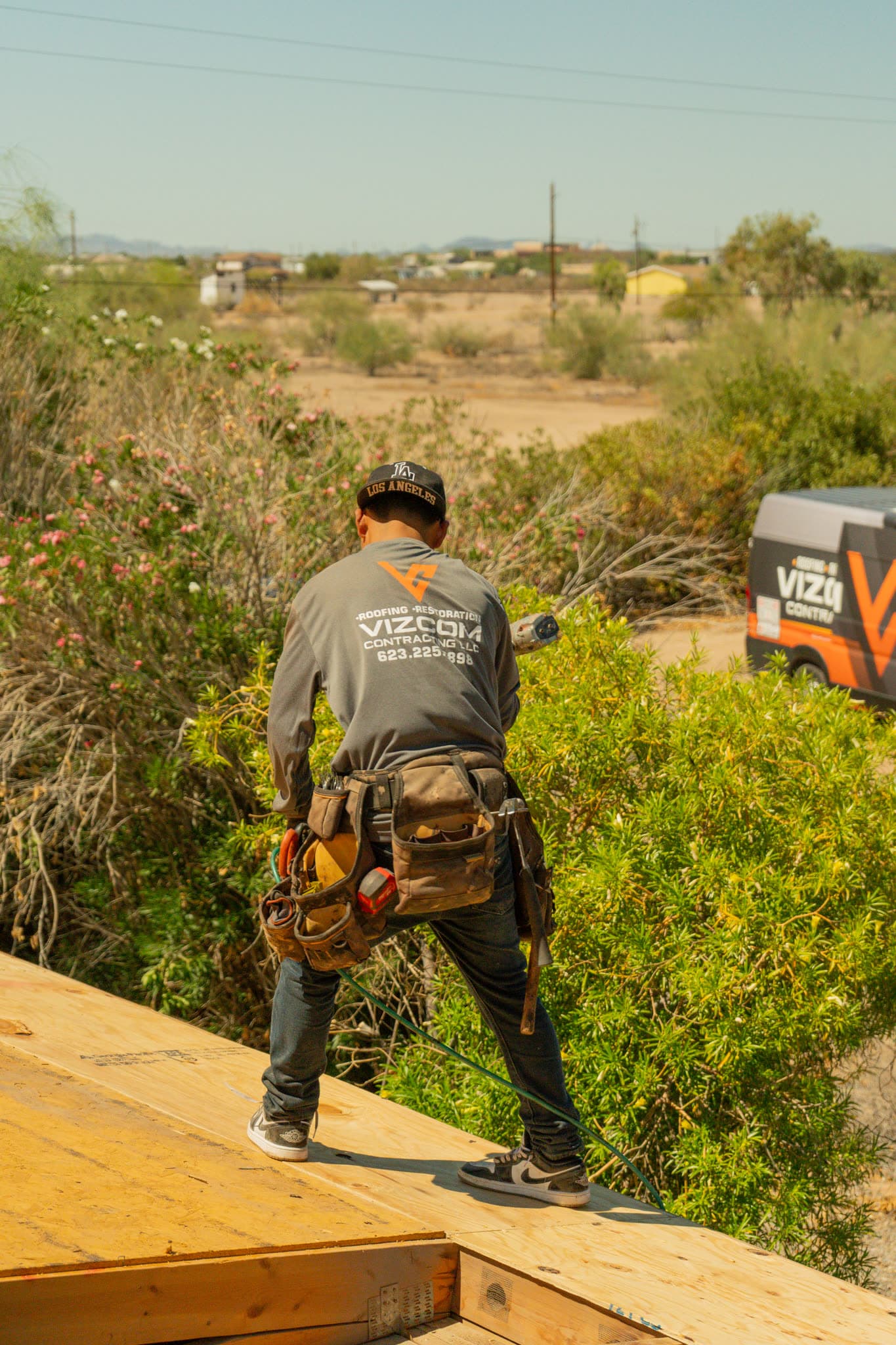 A Vizcom Contracting roofer standing on fresh plywood decking with the company van parked behind the house.