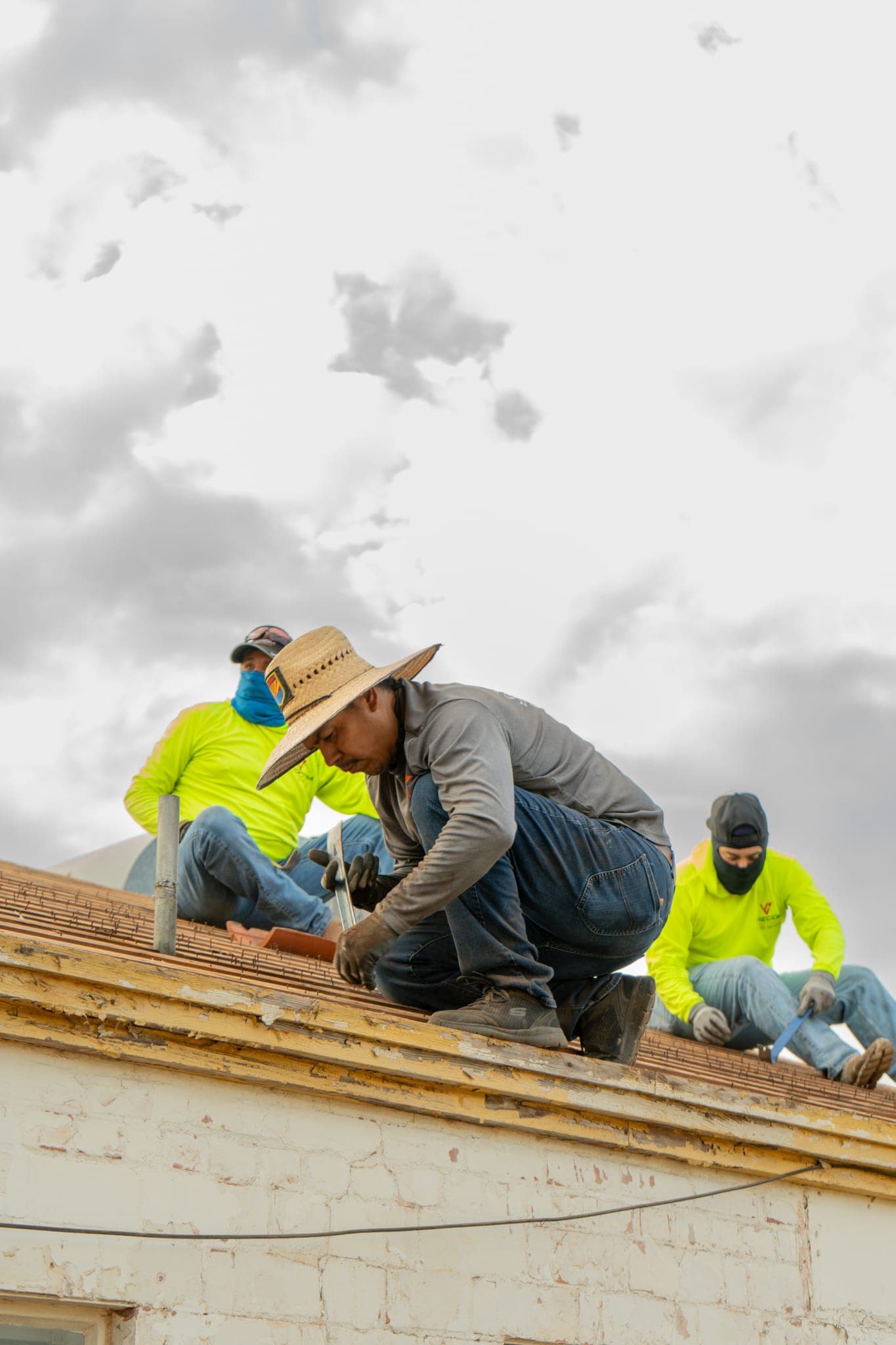Three Vizcom Contracting roofers working along the edge of a roof, cutting away old material down to the wood.